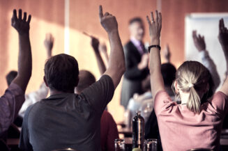 Raised hands and arms of large group of people in class room, audience voting in professional education surrounding, selective focus with anonymous people.